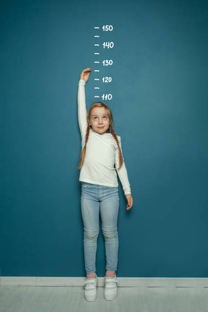 niña midiendo el crecimiento en el fondo de la pared en el hogar. concepto de girl power. - corto longitud fotografías e imágenes de stock