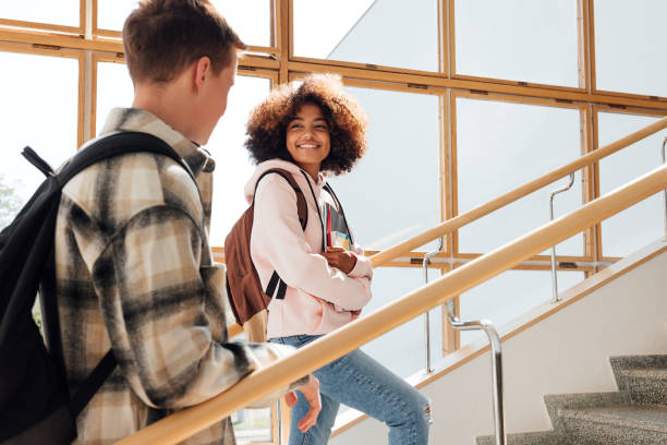 istock Two classmates climbing college stairs. Smiling woman student looking at her classmate on staircase. 1401961349