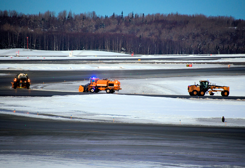 Anchorage, Alaska, USA: snowplow trucks cleaning the tarmac at Ted Stevens Anchorage International Airport, at dawn.