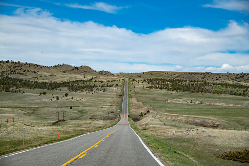 Long, narrow, straight, hilly, Montana highway with no buildings, no wires, no civilization in central Montana in northwestern USA.