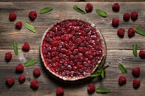 Delicious pie with fresh raspberries on a decorative wooden background with raspberries and mint leaves