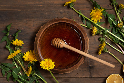 Dandelion honey with dandelion leaves and flowers in a wooden bowl on a black background. Top view.
