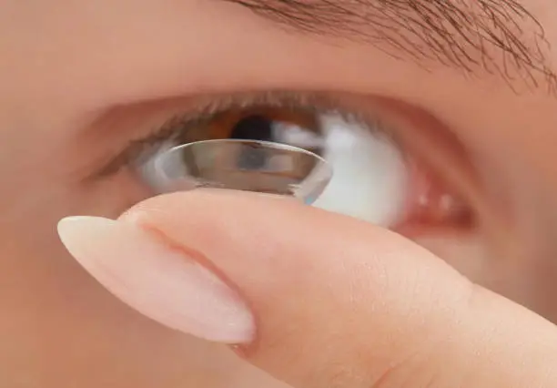 Woman putting soft contact lens into eye. Contact lens on female finger against the background of a blurred eye, close up. Shallow depth of field. Focus on fingertip and contact lens.