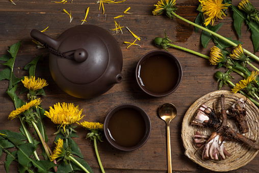 Two cups of dandelion tea with dandelion herb (leaf, flower and root) on a rustic wooden background. Top view.