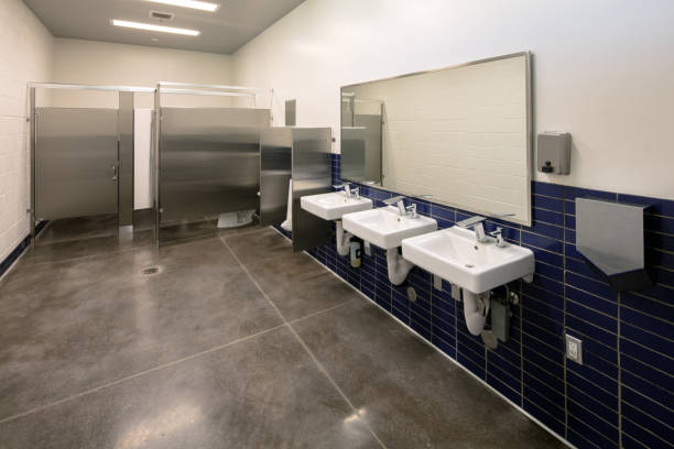 Public School Bathroom with three sinks, mirror, and toilet stalls. No people stock photo