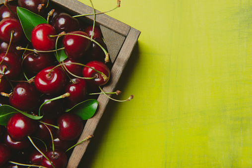 Fresh cherries in a wood container, yellow background.