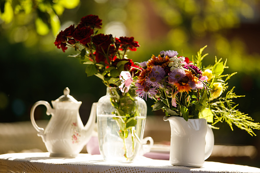 Selective focus shot of vases with flowers set on a table as a decoration for afternoon tea at the back yard.