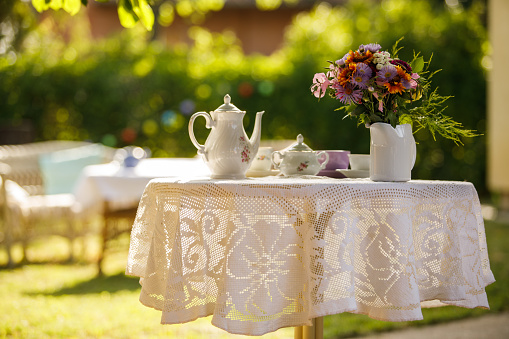 Copy space shot of a cute little set up for afternoon tea, in the sunny back yard, decorated with beautiful bouquet of colorful flowers.