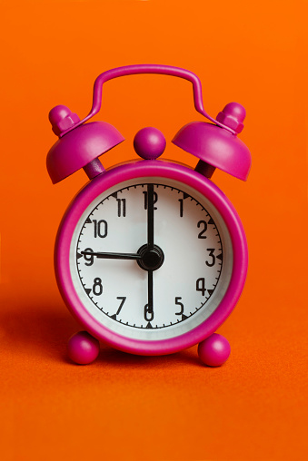 Pink alarm clock on the orange background.