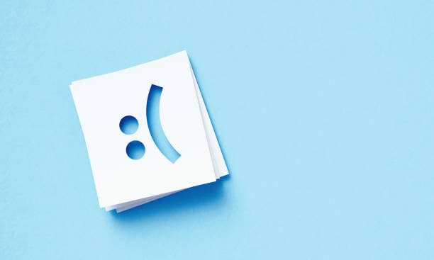White Adhesive Notes With Cutout Sad Face Sitting Over Blue Background White adhesive notes with cutout sad face sitting on blue background. Horizontal composition with copy space. smiley face postit stock pictures, royalty-free photos & images