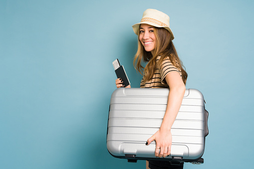 Beautiful Caucasian woman carrying a suitcase and looking ready for a trip in a studio
