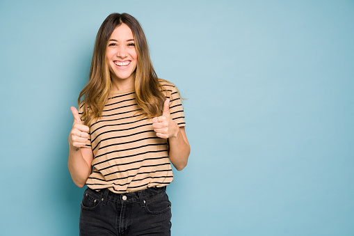 Caucasian woman looking cheerful and holding two thumbs up in a studio with blue background