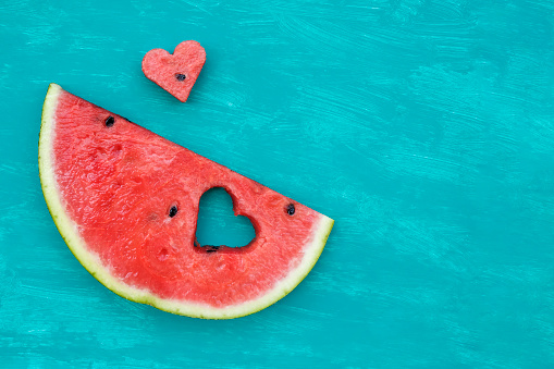 Red watermelon piece with heart on aquamarine background with copy space