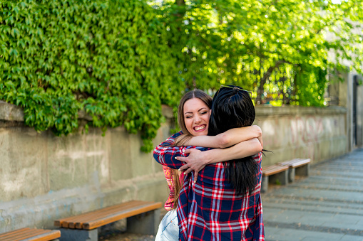 Two happy young girls hug each other outdoors