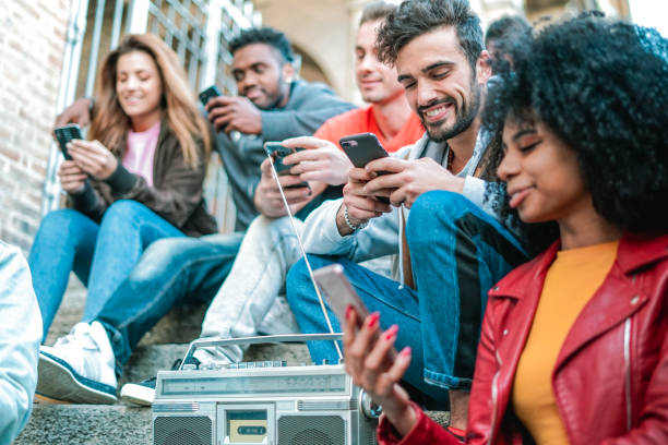 мод�ные люди сидят на лестнице и слушают музыку с винтажным бумбоксом, проверяя свои социальные приложения на смартфоне. - five people audio стоковые фото и изображения
