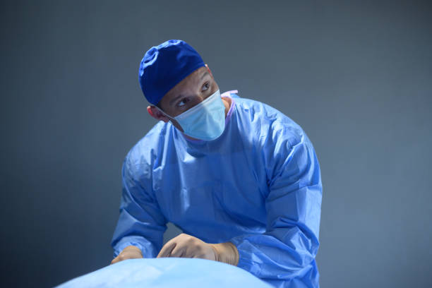 ein chirurg mit operationskittel beschäftigt mit der operation im operationssaal trägt eine chirurgische maske, die auf den monitor schaut - chirurgenbrillen stock-fotos und bilder