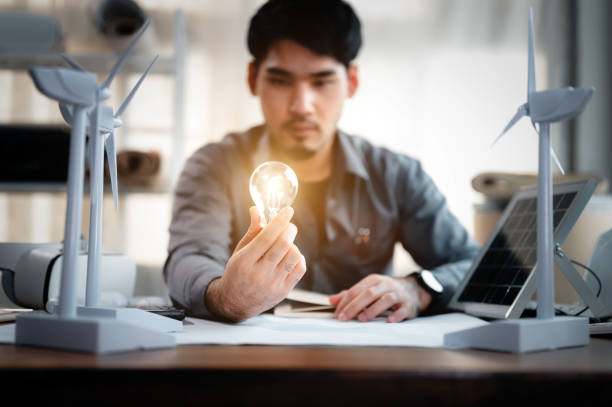 istock Energy engineer holding light bulb in modern office with solar cell sample and wind turbine model, Creative thinking innovative alternative energy design. Saving nature or ecology concept. 1401993095