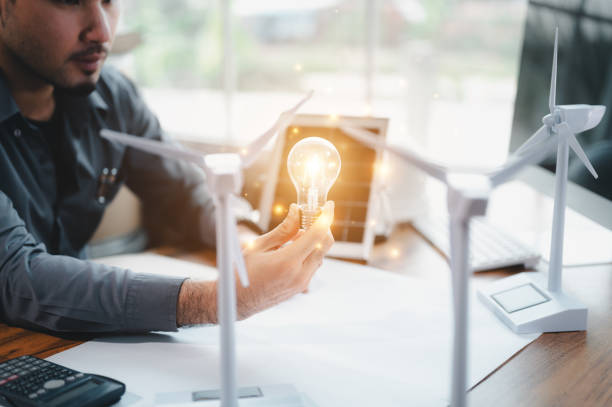 energy engineer holding light bulb in modern office with solar cell sample and wind turbine model, creative thinking innovative alternative energy design. saving nature or ecology concept. - wind turbine fuel and power generation clean industry imagens e fotografias de stock