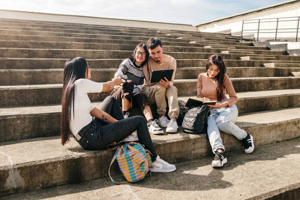 Group of friends studying on a university campus stairway on a sunny day.