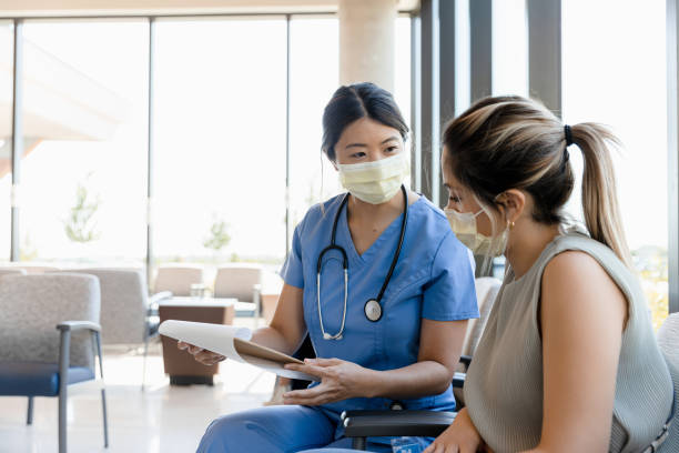 Female nurse asks young woman questions for record In the hospital waiting room, the young adult female surgical nurse asks the young adult woman questions for the medical record. triage stock pictures, royalty-free photos & images