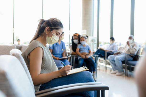 Protective masks are required in the busy hospital waiting room Everyone wears the required protective masks as they wait in the busy hospital waiting room. waiting room stock pictures, royalty-free photos & images