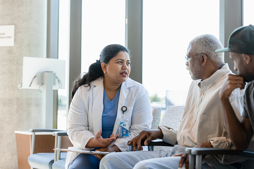 The compassionate mid adult female doctor discusses sensitive medical issues with her senior adult male patient as the young adult son listens in.