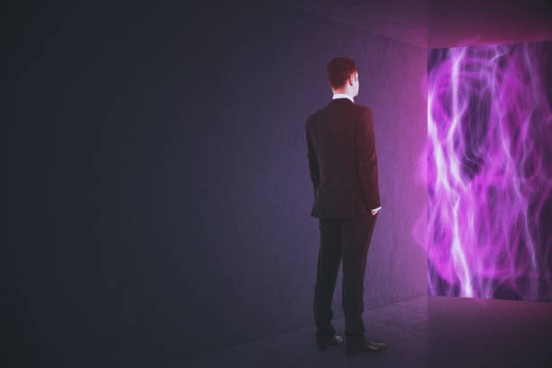 Back view of young businessman standing in abstract interior with bright glowing tech wave window view and mock up place on gray wall. Innovation, metaverse and cyberspace concept