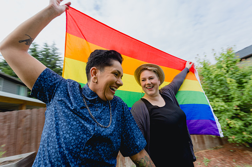 Lifestyle portraits of a happy lesbian couple with a rainbow pride flag over their shoulders.