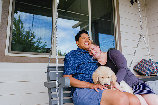 Lesbian couple relaxing on their front porch swing with their cute puppy dog.