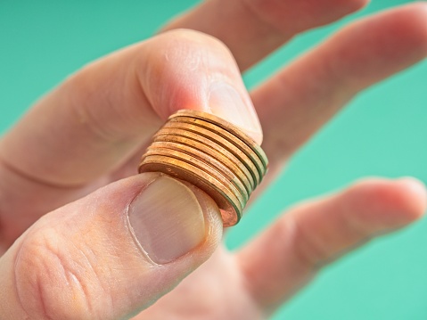 Human hand pinching a stack of pennies, a concept of difficult financial times. Fingers pinch a stack of copper pennies on a green background, a symbol of challenging budgets in a high inflation environment.