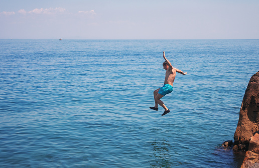 Middle age man enjoying on summer vacations in Greece. He jumping from cliff and diving into blue sea