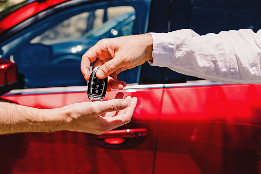 Salesperson giving car keys to the new owner. Close-up of hands on the background of red automobile