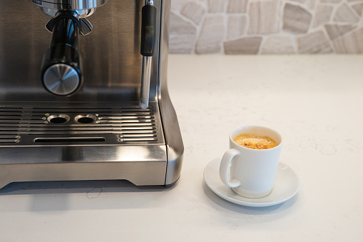 Coffee machine with a cup of espresso sitting on quartz kitchen counter.