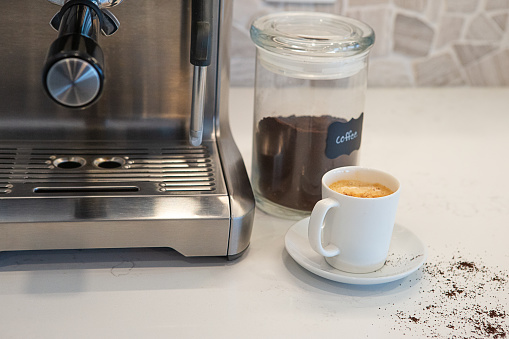 Coffee machine with a cup of espresso sitting on quartz kitchen counter.