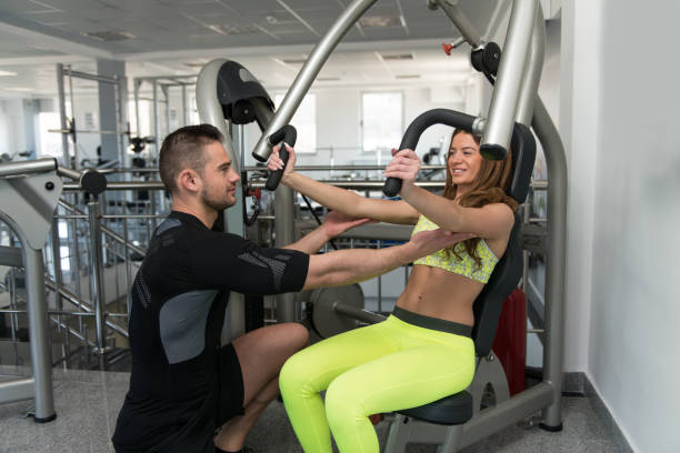 istock Woman Train Chest On Machine With Personal Trainer 1402016631
