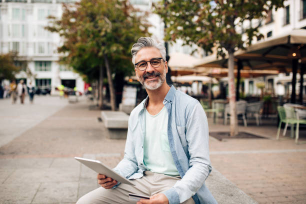 Portrait of a mature man on vacation taking a break and using tablet in the city stock photo
