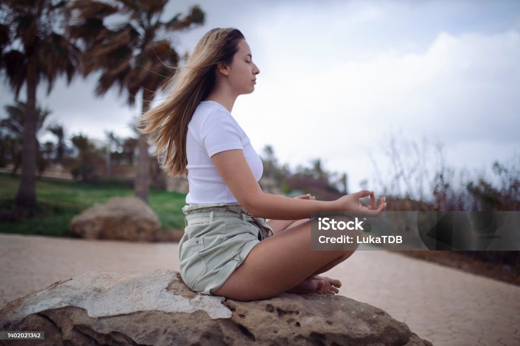 A side view of a woman meditating and thus relaxing her mind and body. A woman meditates and tries to stay stress-free from social media and more. 25-29 Years Stock Photo