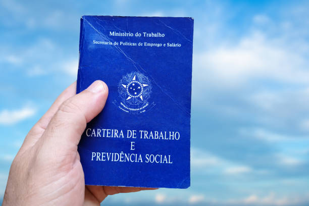 istock Man's hand holding Brazilian Work Card isolated on background with blue sky. Written in Portuguese Federative Republic of Brazil, Ministry of Labor. Work and Social Security card. Brazilian work concept 1402021455