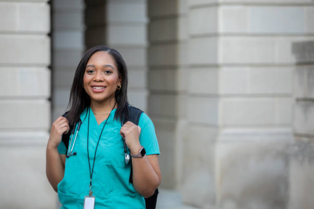 Young African American woman smiles while walking on campus of medical school or nursing college stock photo