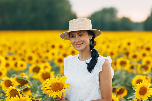 Beautiful young woman portrait in a hat on a field of sunflowers