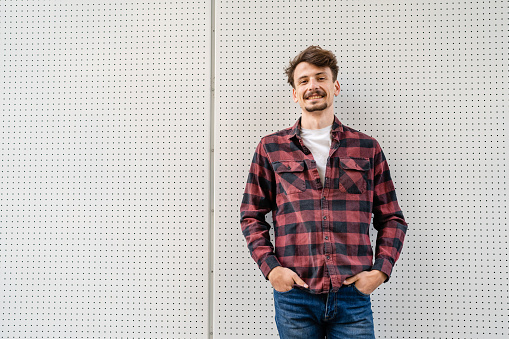 One young caucasian man with brown hair and mustaches wearing shirt looking to the camera modern happy adult male smile portrait in front of white wall copy space waist up
