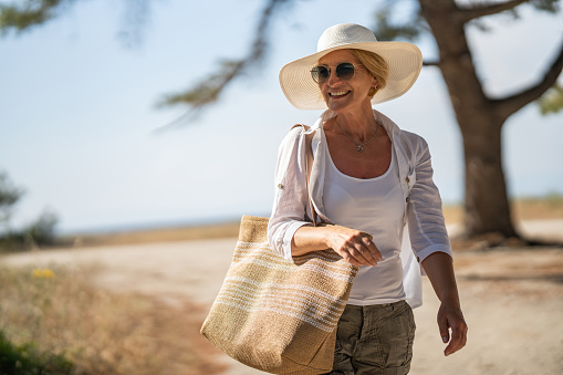 Mature woman carrying a bag, she is walking back from the beach.