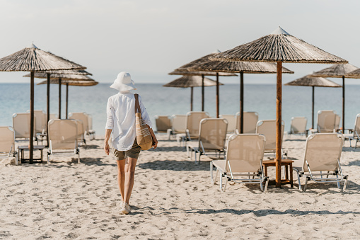 Mature woman carrying a bag is arriving at the beautiful sandy beach.