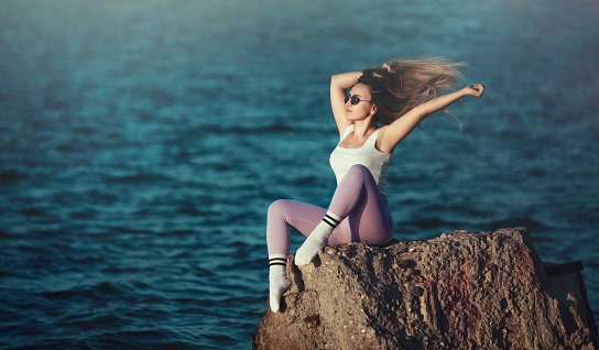 young fit woman standing on a rock in the sea.her hair blows in the wind