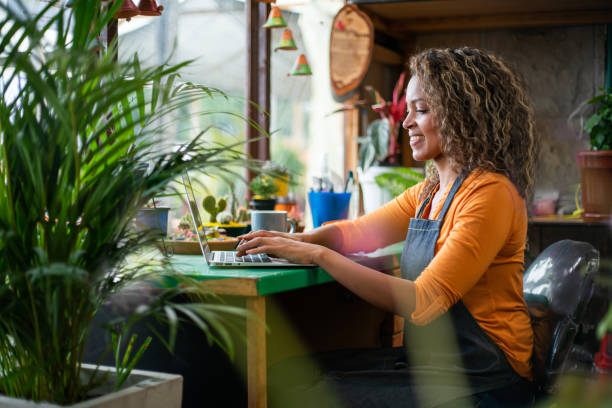 mujer trabajando en una computadora portátil en su floristería - florist small business flower shop owner fotografías e imágenes de stock