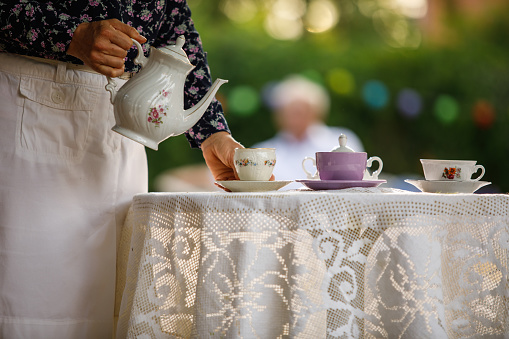 Woman pours tea from a glass teapot into a glass Cup. Tea party in the open air. Close-up of a Cup and teapot in nature in the forest