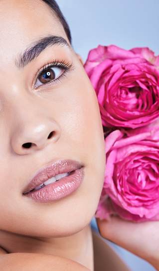Studio portrait of a beautiful mixed race woman posing with a flower. Young hispanic using an organic skincare treatment against a blue copyspace background