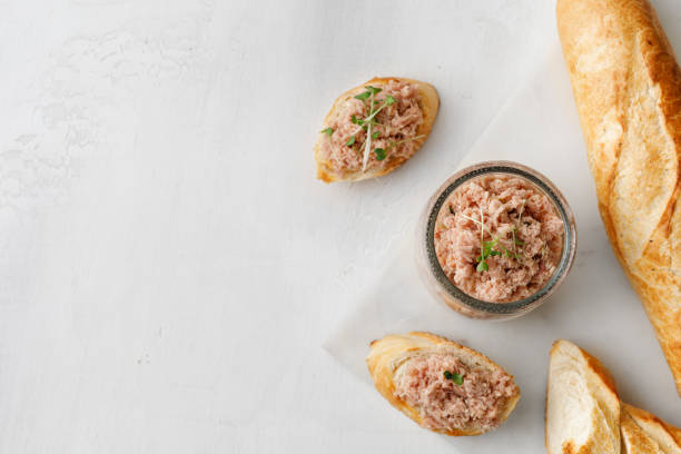 Toast with tuna on baguette. Healthy tuna pate or rillettes in a glass jar on marble board and white background. Top view. Toast with tuna on baguette. Healthy tuna pate or rillettes in a glass jar on marble board and white background. Top view. tuna pate stock pictures, royalty-free photos & images
