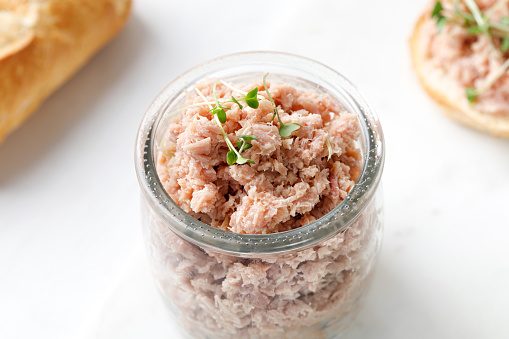 French tuna fish rillettes or pate with micro greens in glass jar and white background. Close up, copy space