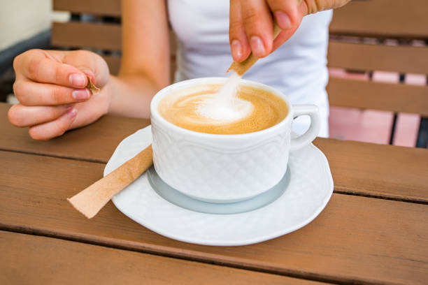 istock girl scattering sugar in cappuccino close-up. 1402056905